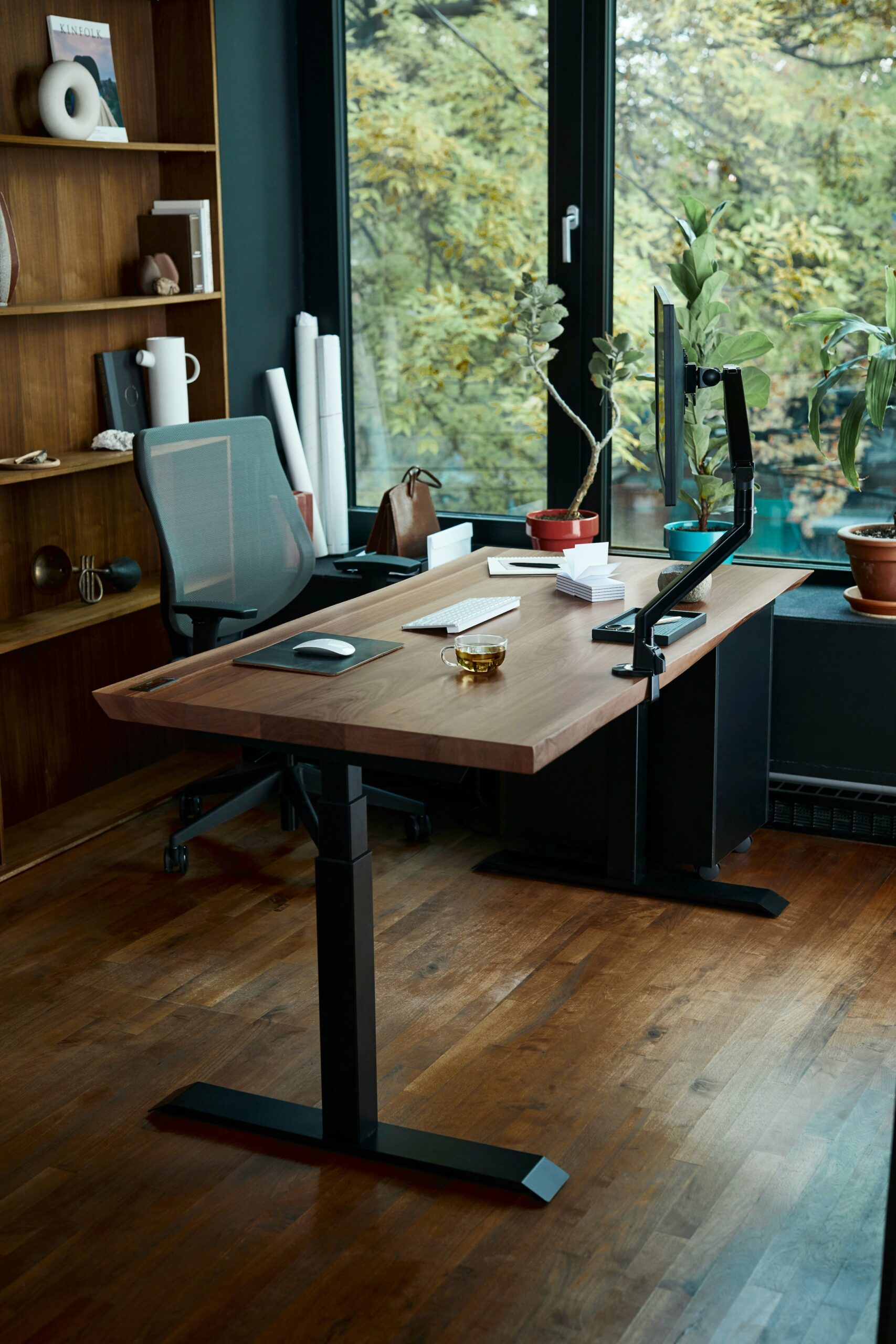 A wooden standing desk beside a window overlooking trees